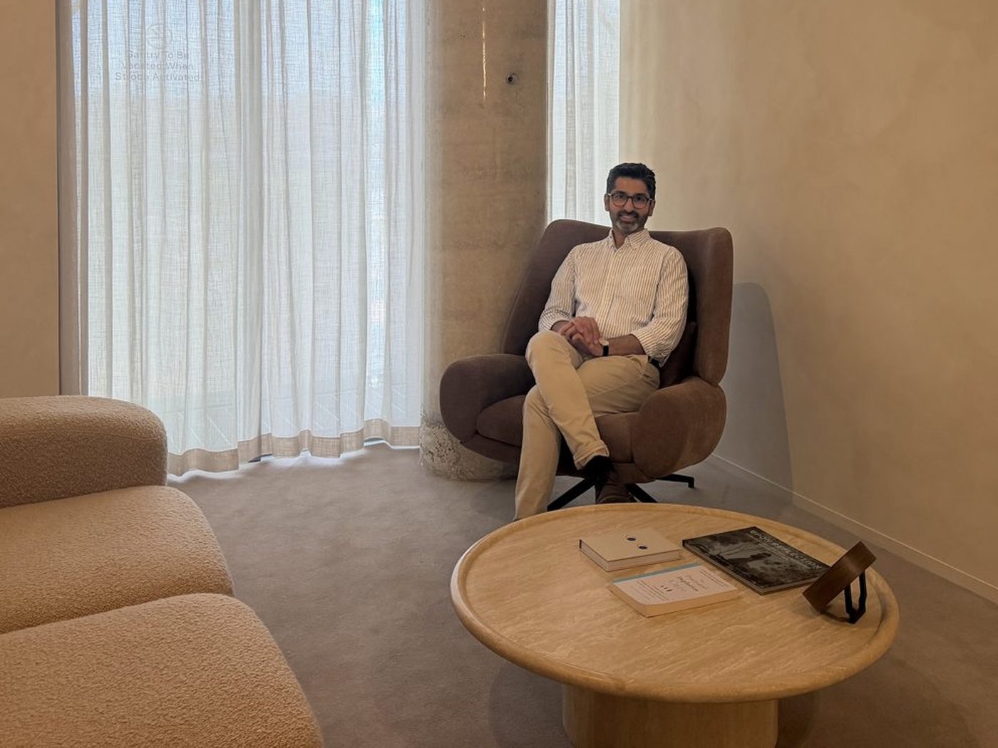 Dr Bharat Visa seated in the consulting room beside a boucle sofa and round travertine table